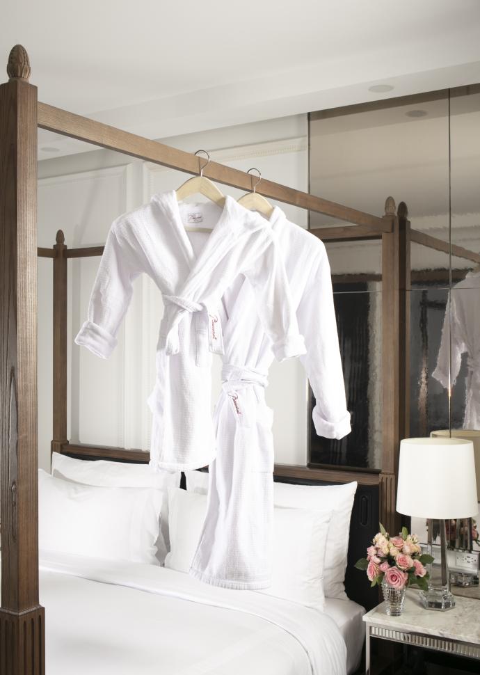 To hvide badekåber, en lang og en kort, hænger på sengestolpen i en Baccarat Hotel