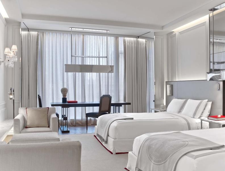 Una habitación de hotel decorada principalmente en tonos blancos, con dos camas y dos sillones