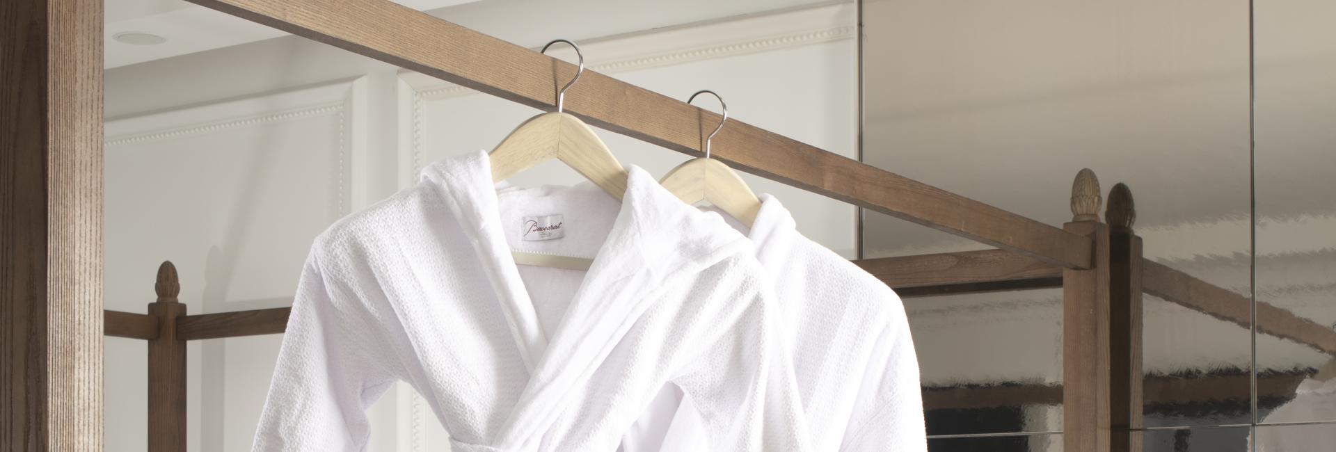 Twee witte badjassen, een lange en een korte, hangen aan het bedhoofdeinde in een Baccarat Hotel