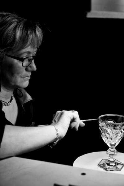 A crystal wine goblet is gilded by hand using a paintbrush.