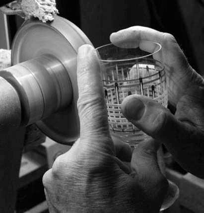 A crystal wine glass carefully being etched on the wheel.