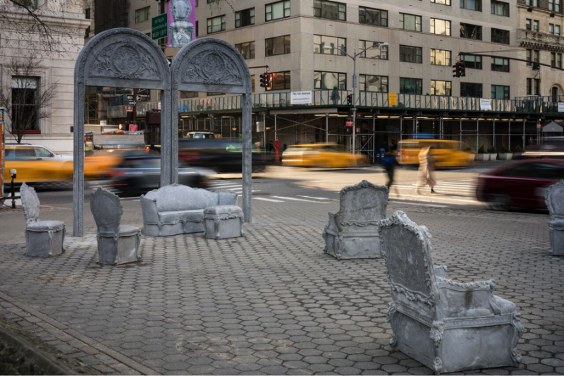 Concrete furniture and arches created by artist Liz Glynn sit in a cobblestone plaza in New York.