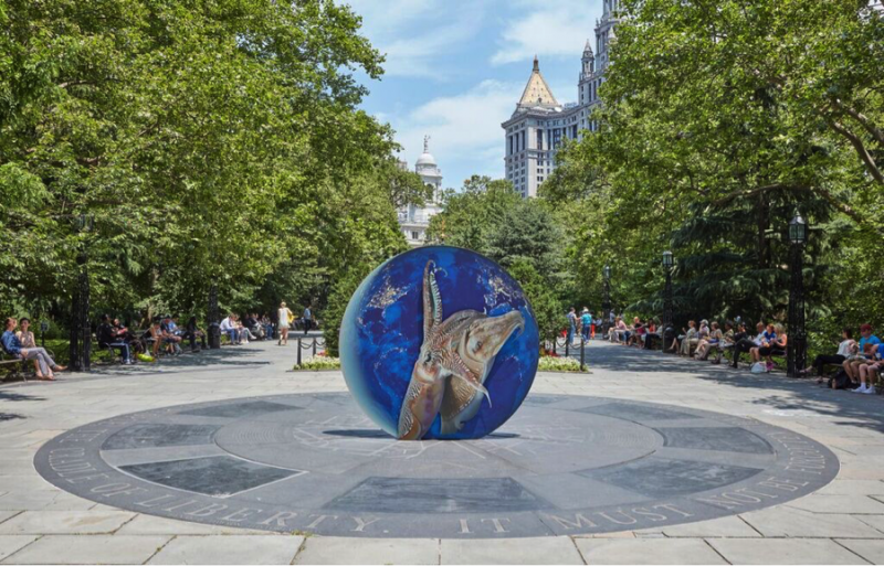 A large aluminum sculpture of a blue orb featuring two large squids sits in the middle of City Hall Park in New York.