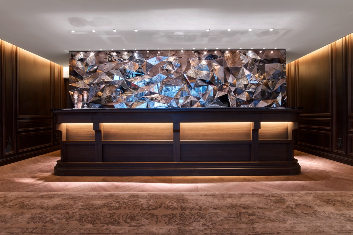 Baccarat reception desk beneath faceted mirrored art wall, with dark wood paneling and patterned area rug flooring