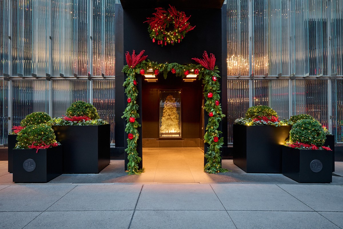 Baccarat Hotel Entrada decorada con una guirnalda festiva, una corona roja y topiarios, que enmarcan el árbol dorado iluminado del interior.