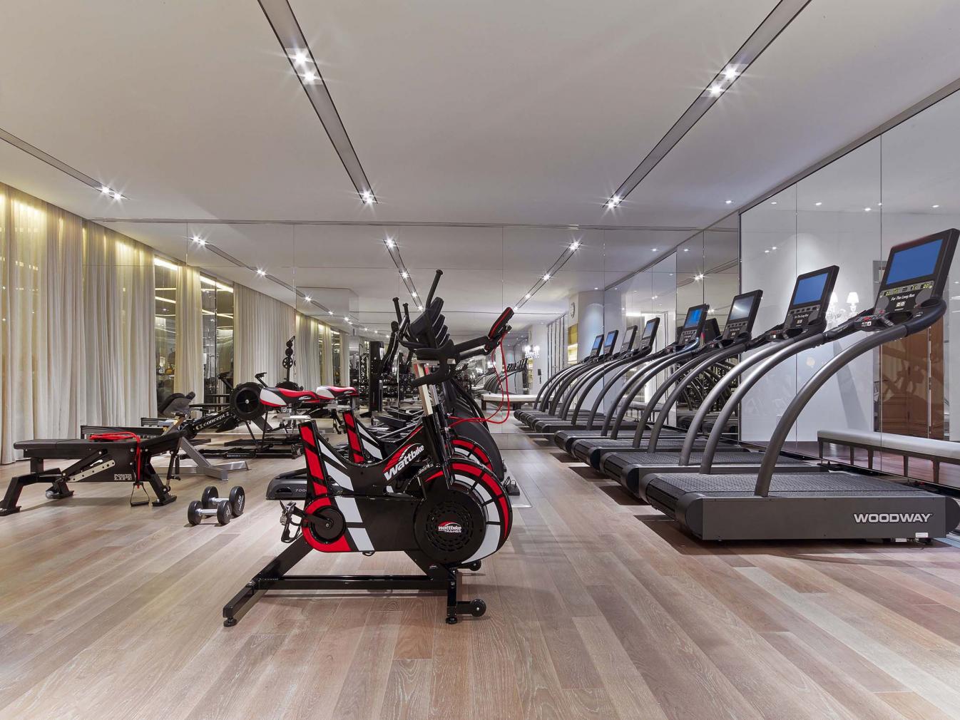 Exercise benches, row machines, stationary bicycles, and treadmills are situated from left to right, within the Baccarat's fitness facility