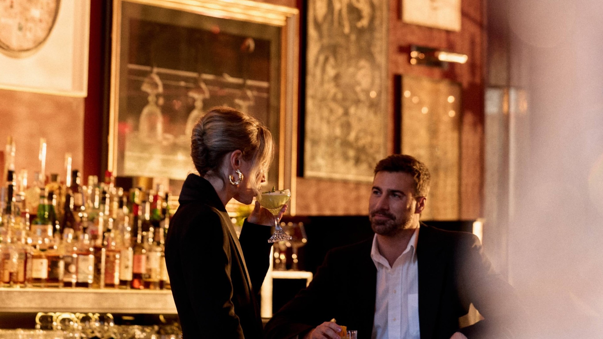A man and woman sit at a bar, enjoying drinks and engaged in conversation