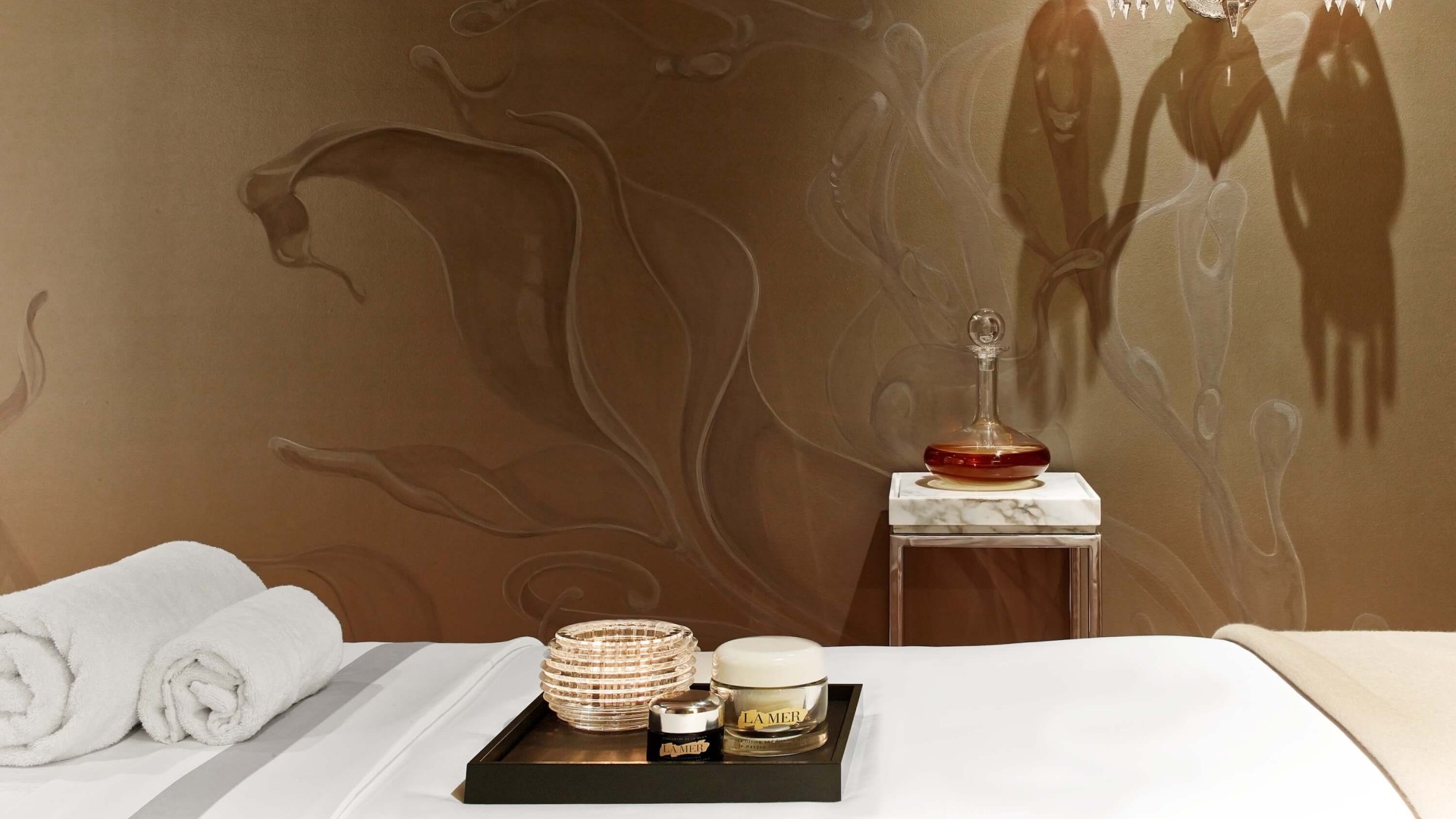 A neatly made bed with a wooden tray on top, featuring a lamp and decorative items