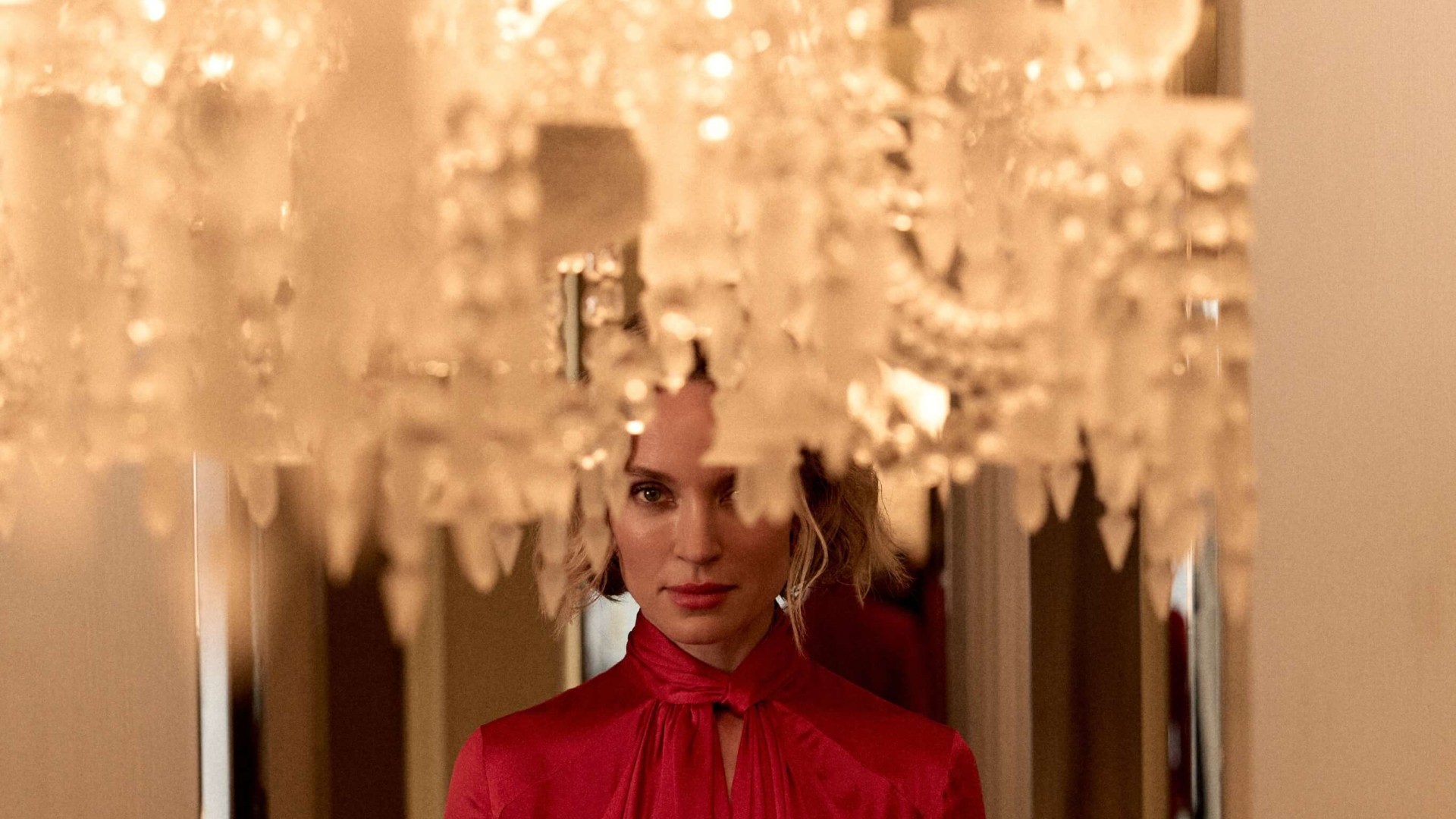 A woman in a red dress poses elegantly in front of a sparkling chandelier