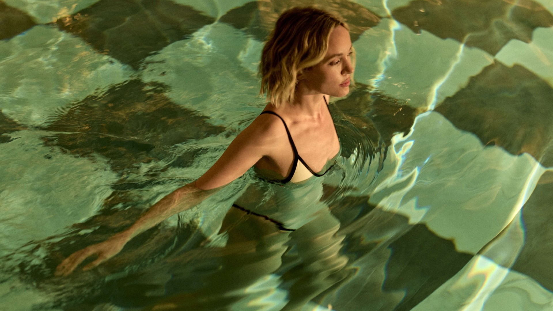 A woman in a swimsuit enjoys a sunny day while swimming in a clear blue pool.