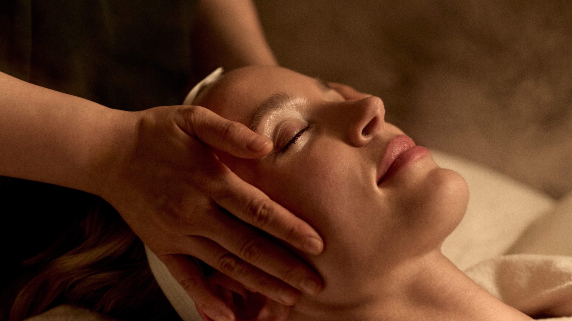 A woman receiving a facial massage at a spa, relaxing with her eyes closed and a serene expression on her face
