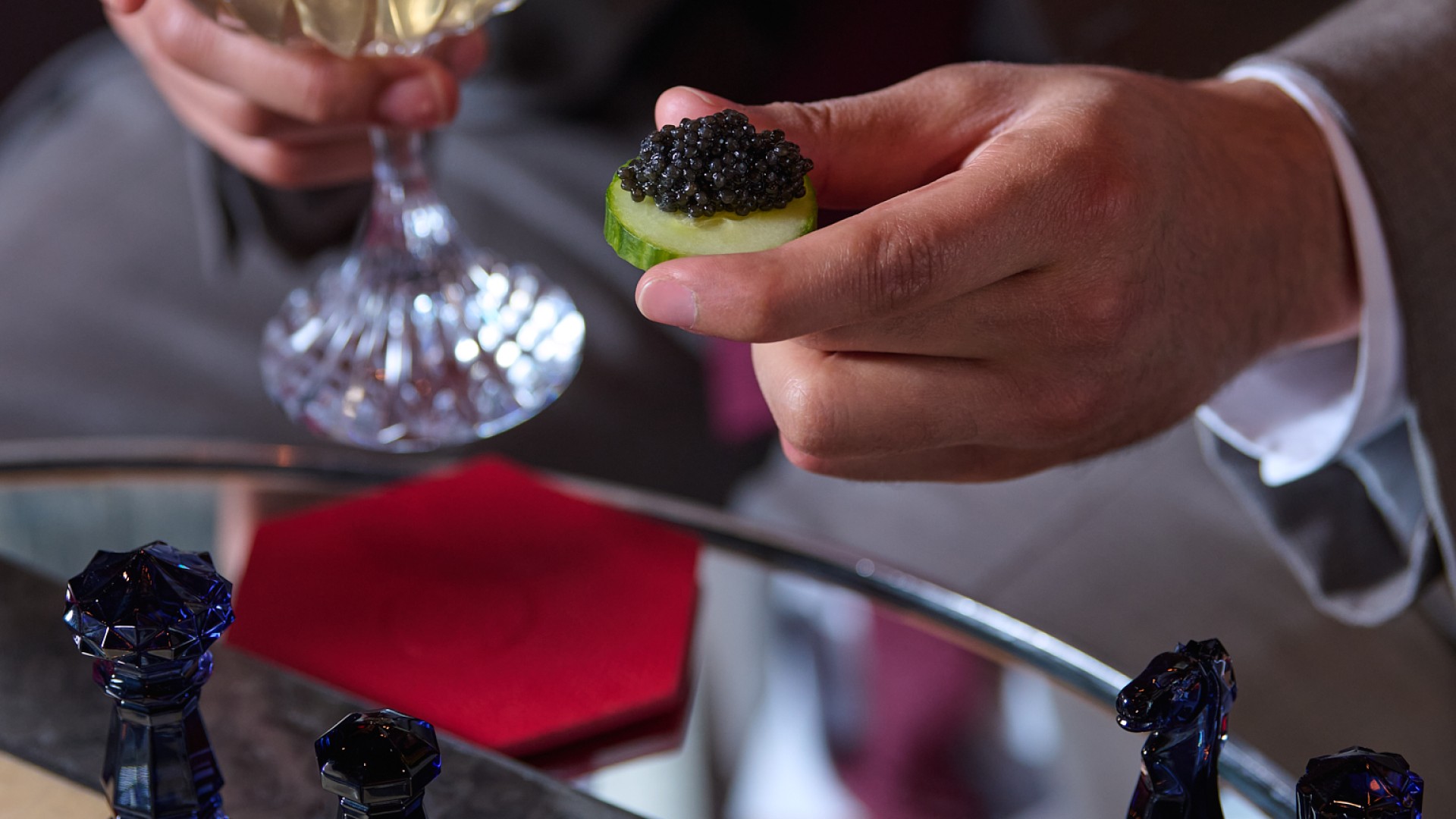 A man holding a canape and a cocktail looking at a chess board