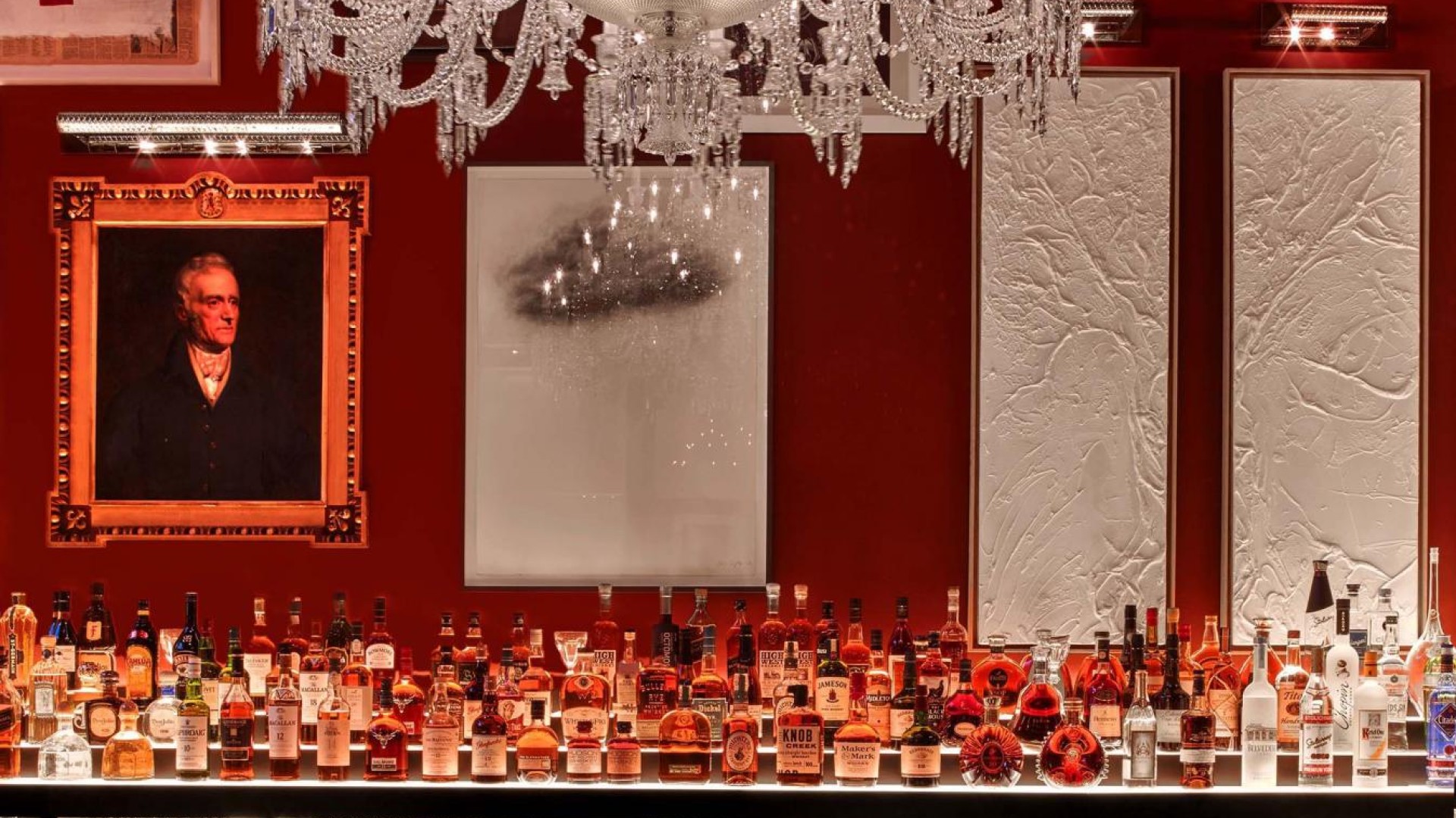 A red bar featuring an elegant chandelier and a large decorative mirror on the wall.
