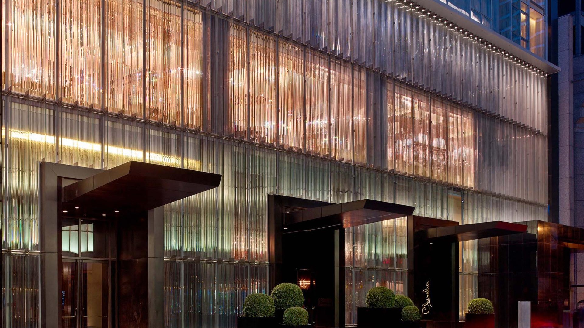 El hotel, con una fachada elegante y una entrada llamativa, se alza con el bullicioso paisaje urbano como telón de fondo.