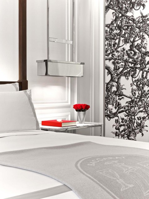 A white bed adorned with red pillows, set against a black and white floral wallpaper backdrop.
