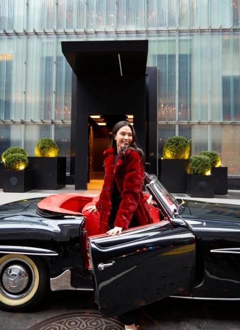 A woman wearing a red coat is seated in a classic car