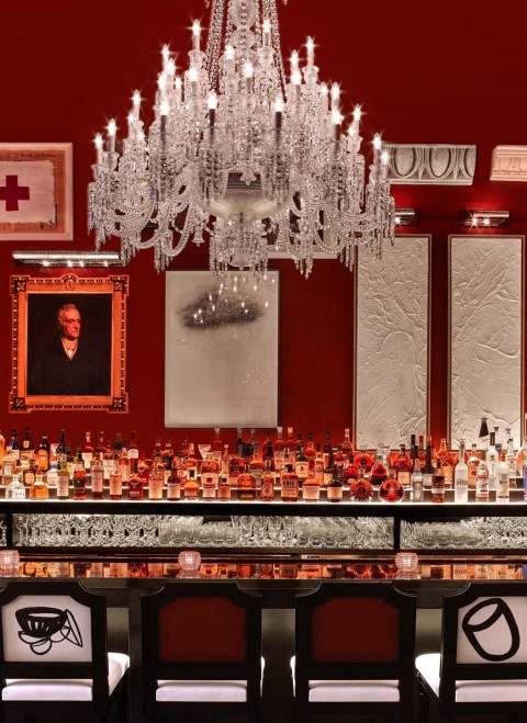 A red bar featuring an elegant chandelier and a large decorative mirror on the wall.