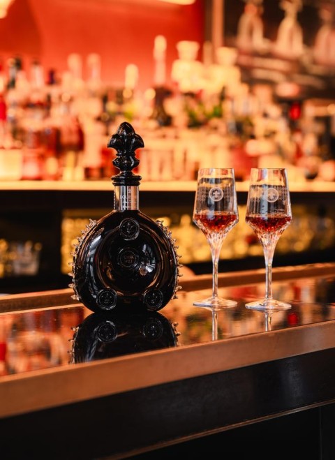 A bottle of liquor with two glasses on a polished bar surface, creating an inviting atmosphere for socializing