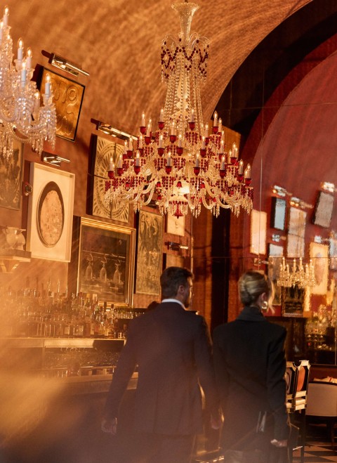 Two people dressed in suits stroll through a dimly lit bar, creating a sense of sophistication and mystery