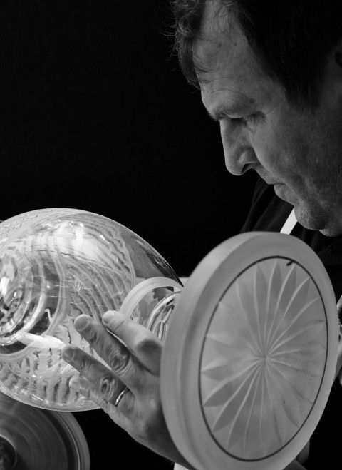 A man shapes a glass vase using a large bowl as part of the glassblowing process