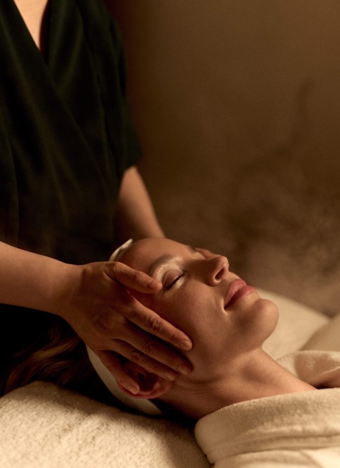A woman receiving a facial massage at a spa, relaxing with her eyes closed and a serene expression on her face