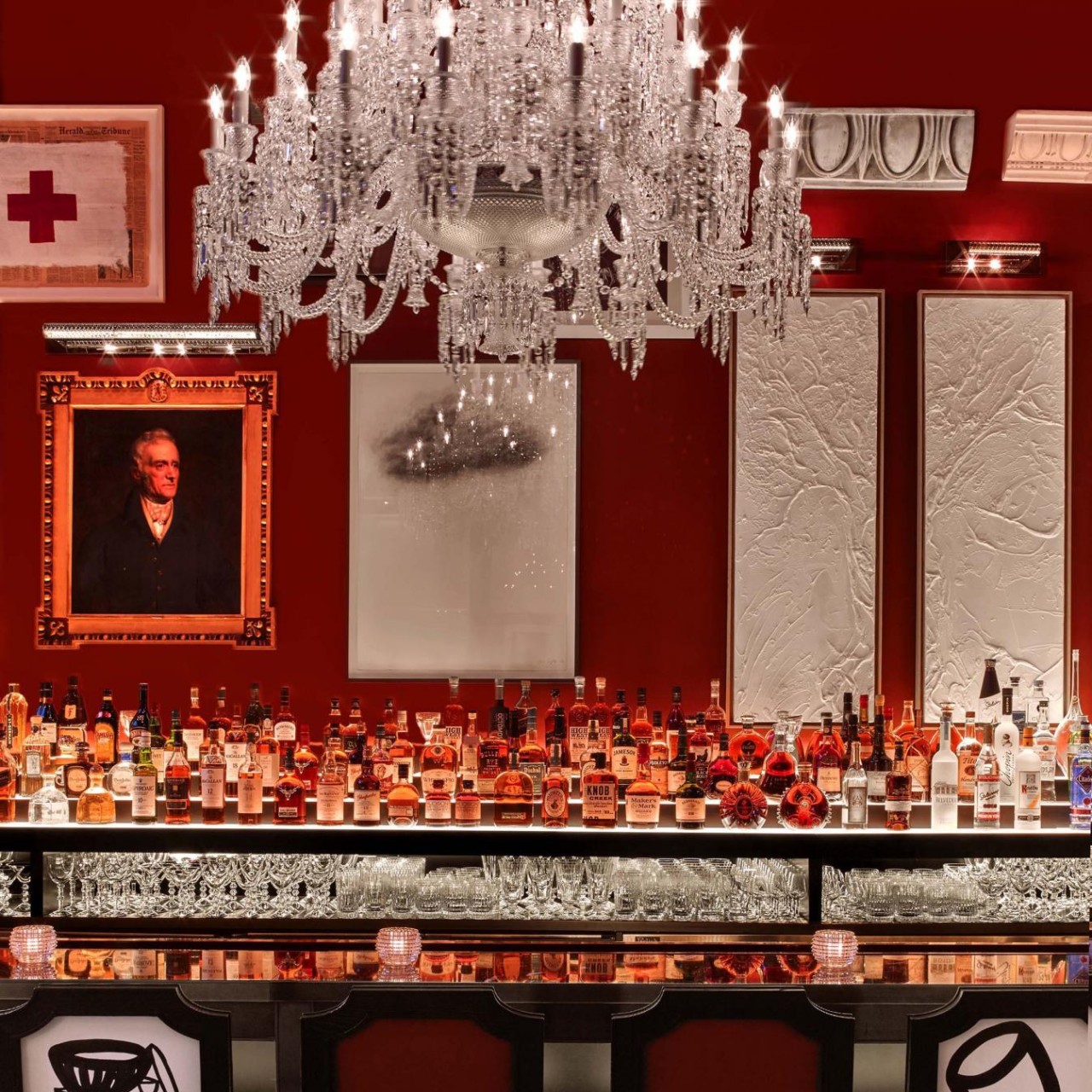 A red bar featuring an elegant chandelier and a large decorative mirror on the wall.