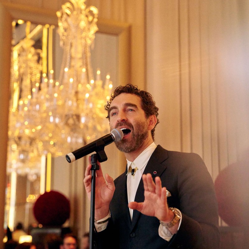 A man in a suit passionately sings into a microphone on stage