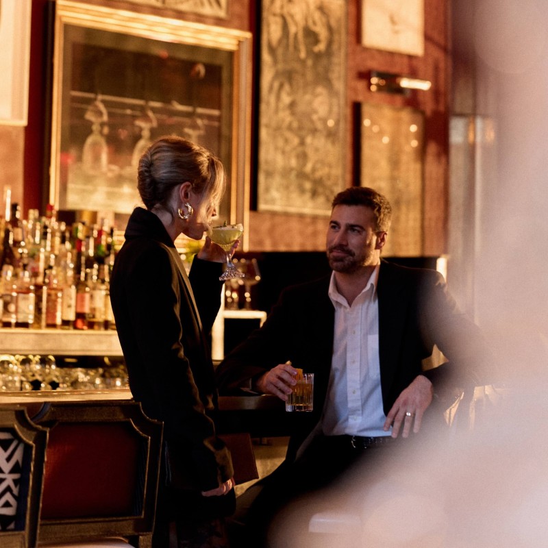 A man and woman sit at a bar, enjoying drinks and engaged in conversation