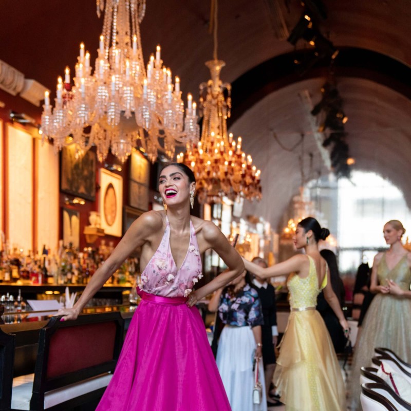 A woman in a pink dress poses gracefully in front of an elegant chandelier