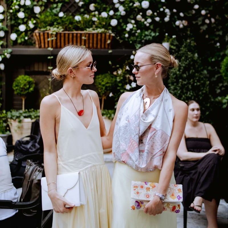Two women wearing stylish dresses pose together, showcasing their outfits in a cheerful outdoor environment