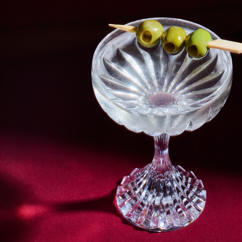 A martini glass filled with a clear beverage, garnished with olives on the rim