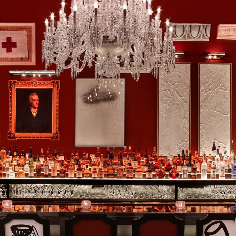 A red bar featuring an elegant chandelier and a large decorative mirror on the wall.