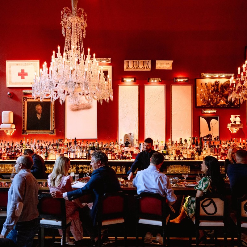 A vibrant red bar scene featuring patrons seated at tables, enjoying drinks and socializing