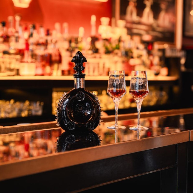 A bottle of liquor with two glasses on a polished bar surface, creating an inviting atmosphere for socializing