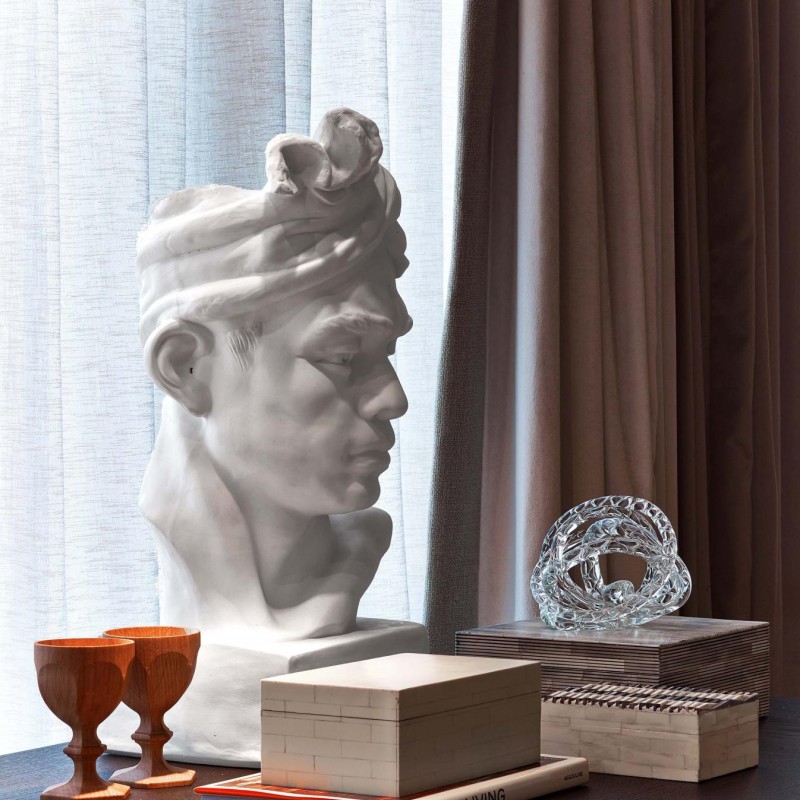 A white marble bust of a man displayed on a wooden table, showcasing intricate facial details and a classical style
