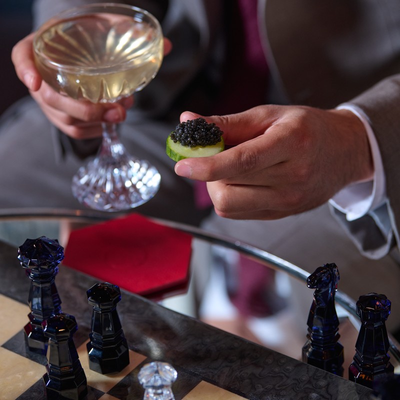 A man holding a canape and a cocktail looking at a chess board